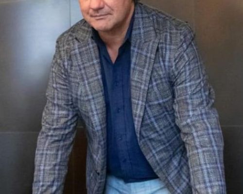 L'immagine mostra tre uomini in posa davanti a uno schermo su cui è proiettato il logo "NEXXT PRESENTA", caratterizzato da colori che richiamano il tricolore italiano. L'uomo a sinistra indossa un abito scuro con camicia bianca, quello al centro un blazer beige con camicia bianca, mentre quello a destra veste un maglione nero con motivi geometrici e una sciarpa. Sullo sfondo è visibile un banner verticale con la scritta "Confartigianato", suggerendo un evento legato all'imprenditoria o al commercio. L'ambiente appare come una sala conferenze o un luogo di presentazione formale.