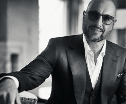 Massimiliano Mazzei - Manager of Us Company Advisor - Black and white portrait of Massimiliano Mazzei elegant with short beard, sunglasses and a three-piece tailored suit with white shirt. His smile and relaxed posture convey confidence and leadership. Us Company Advisor supports Italian entrepreneurs in expanding their business in the United States with personalized strategies.