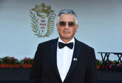 Giosuè Gilberto Di Molfetta - Gerente de Us Company Advisor - Retrato profesional de un hombre con cabello canoso, gafas de sol y esmoquin negro con pajarita, en un contexto elegante con un escudo nobiliario al fondo. La atmósfera exclusiva y el aspecto sofisticado transmiten autoridad y prestigio. Us Company Advisor ofrece consultoría de alto nivel para empresas italianas que quieran expandirse al mercado estadounidense.