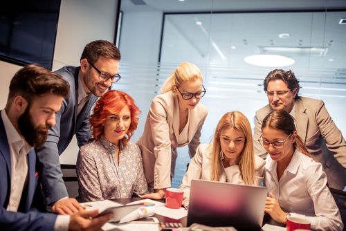 Sales Network Establishment and Management in the USA - The image shows a team of professionals in a modern office, gathered around a laptop, collaborating on sales strategies. The dynamic atmosphere reflects the planning and expansion of commercial networks. Us Company Advisor helps Italian companies develop and manage sales networks in the United States, providing advice on agents, distributors and commercial expansion strategies.