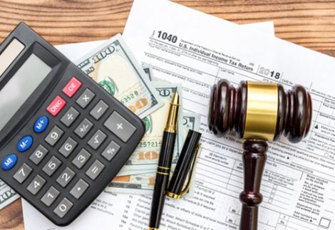 Gestione fiscale e conformità legale per aziende negli USA - L'immagine raffigura documenti fiscali ufficiali statunitensi (U.S. Individual Income Tax Return 1040), una calcolatrice, banconote da 100 dollari, penne e un martelletto da giudice su una scrivania in legno. Questa composizione rappresenta la gestione delle tasse, la conformità legale e il supporto amministrativo. Us Company Advisor assiste le aziende italiane nella fiscalità, apertura di conti bancari e conformità alle normative negli Stati Uniti.
