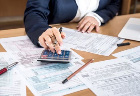 Consulenza fiscale e amministrativa per aziende negli USA - L'immagine mostra una professionista in giacca elegante che utilizza una calcolatrice e compila documenti fiscali ufficiali su una scrivania. Penne e fogli compilati evidenziano l'attenzione ai dettagli nella gestione delle tasse e delle pratiche burocratiche. Us Company Advisor assiste le aziende italiane nell'apertura e gestione fiscale di società negli Stati Uniti, garantendo conformità alle normative americane.